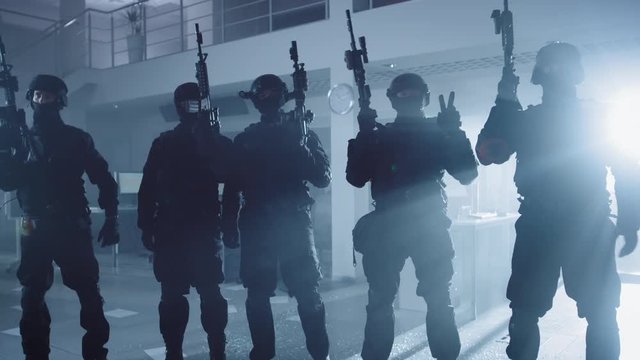 Masked Team of Armed SWAT Police Officers with Rifles are Posing After a Successful Office Building Siege. Soldiers Stand in a Row and Raise Firearms Up in the Air.