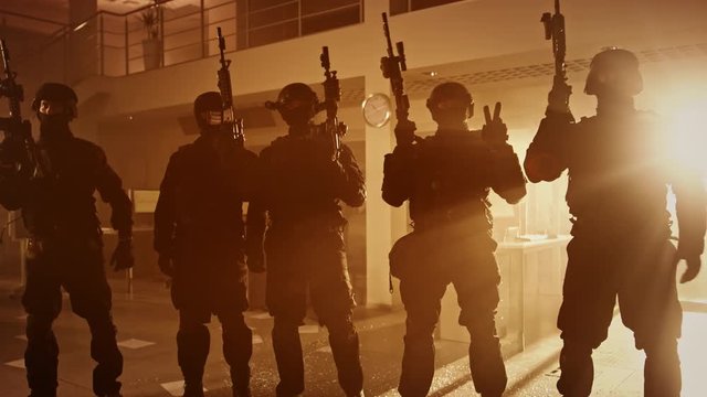 Masked Team of Armed SWAT Police Officers with Rifles are Posing After a Successful Office Building Siege. Soldiers Stand in a Row and Raise Firearms Up in the Air. Warm Color Grading.