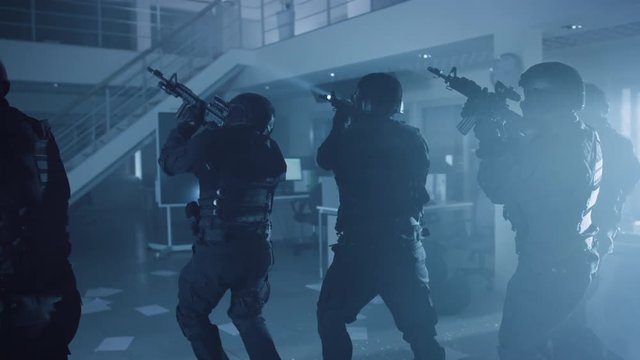 Masked Team of Armed SWAT Police Officers Slowly Move in a Hall of a Dark Seized Office Building with Desks and Computers. Soldiers with Rifles and Flashlights Surveil and Cover Surroundings.