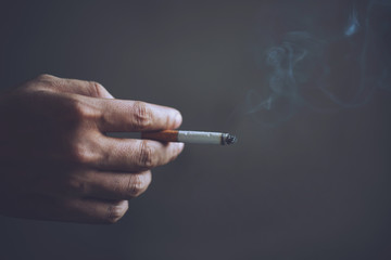 man holding smoking a cigarette in hand. Cigarette smoke spread. dark background