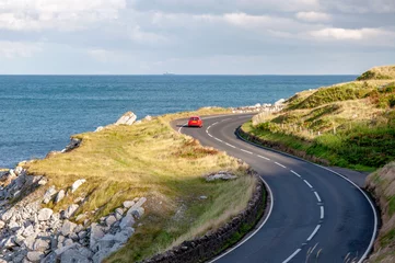 Photo sur Plexiglas Atlantic Ocean Road La côte est de l& 39 Irlande du Nord et Antrim Coastal Road, alias Causeway Coastal Route avec une voiture rouge. Lumière du coucher du soleil