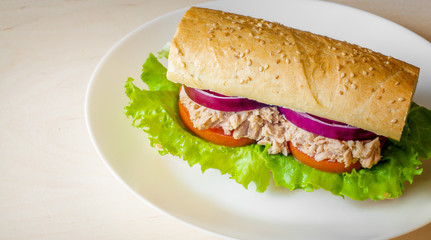 Tuna sandwich on wooden table. White plate. Tuna, lettuce, onion, tomato, bread. Free space.