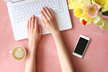 Top view shot of woman typing on white laptop computer, concrete textured table background. Feminine workspace with flowers bouquet. Close up, copy space.