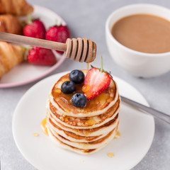 Honey pours on the stack of pancakes with berries Croissant and coffee breakfast