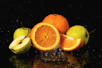 Fototapeta na wymiar Apples and oranges fruits with drops and splashes of water on a black background