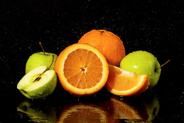 Fototapeta na wymiar Apples and oranges fruits with drops and splashes of water on a black background