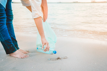 Woman's hand picking up plastic bottle garbage by the beach. Volunteering concept.