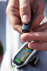 Woman using lancelet on finger, close up view of human hands with a glucometer