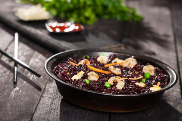 Cooked black rice with shrimps and vegetables in a dish on the wood background.