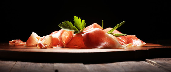 Italian prosciutto crudo or jamon with rosemary. Raw ham on wooden board