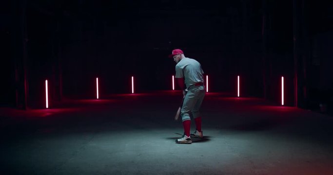 WIDE FIXED Caucasian professional baseball player batter posing against dark background in a large abandoned warehouse. 4K UHD 60 FPS SLOW MOTION