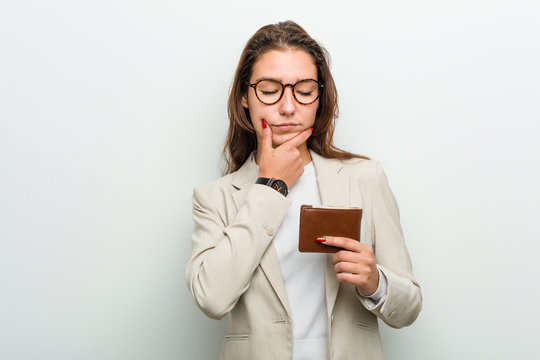 Young european business woman holding a wallet looking sideways with doubtful and skeptical expression.