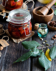 Two glass jars with homemade canned plums jam, marmalade, jelly on rustic wooden table with cardamon, cinnamon,  anise, bowl of plums
