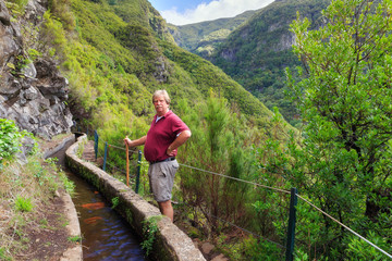 Beautiful landscape view of a senior tourist on the hiking path in nature on the green island Madeira, during a hike on a trail along a famous levada