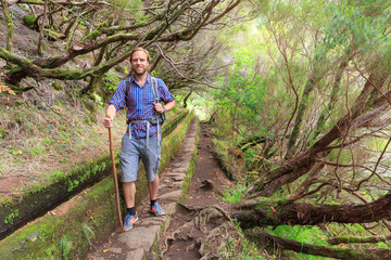 Obraz premium Beautiful landscape view of a young handsome tourist on the hiking path in nature on the green island Madeira, during a hike on a trail along a famous levada