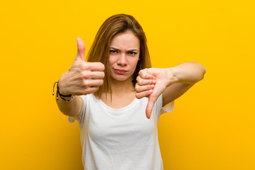 Young natural caucasian woman showing thumbs up and thumbs down, difficult choose concept