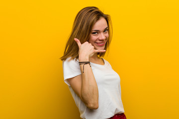 Young natural caucasian woman showing a mobile phone call gesture with fingers.