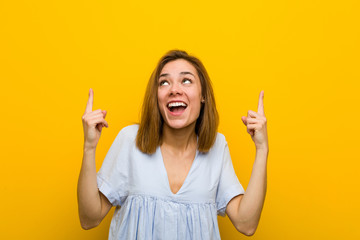 Young pretty young woman indicates with both fore fingers up showing a blank space.