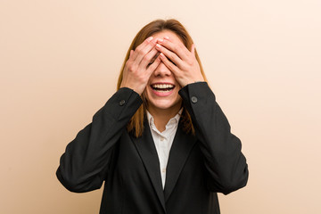 Young caucasian business woman covers eyes with hands, smiles broadly waiting for a surprise.