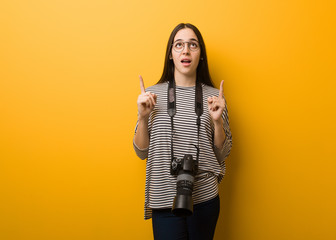 Young photographer woman surprised pointing up to show something