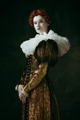 Having doubts. Medieval redhead young woman in golden vintage clothing as a duchess standing...