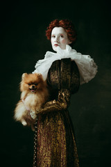Brilliance view. Medieval redhead young woman in golden vintage clothing as a duchess holding puppy...