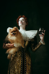 Delicious. Medieval redhead young woman in golden vintage clothing as a duchess holding puppy and...