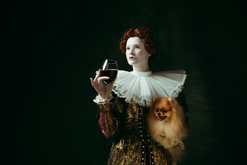 Wishes. Medieval redhead young woman in golden vintage clothing as a duchess holding puppy and...