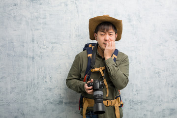 Young chinese explorer man holding a camera biting nails, nervous and very anxious