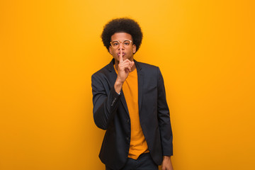 Young business african american man over an orange wall keeping a secret or asking for silence