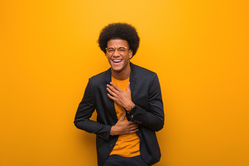 Young business african american man over an orange wall laughing and having fun