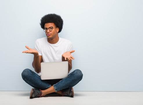 Young Black Man Sitting On The Floor With A Laptop Confused And Doubtful