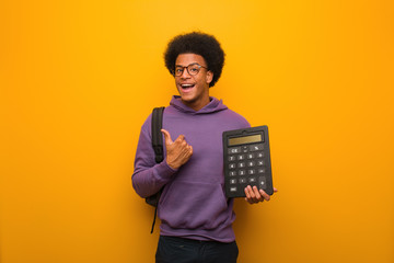Young african american student man holding a calculator surprised, feels successful and prosperous - obrazy, fototapety, plakaty