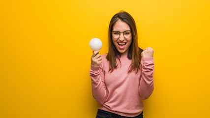 Young cute woman holding a light bulb surprised and shocked