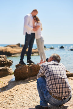 photographer and couple in love, beach photo shooting at sunny day, man taking pictures of young woman and man