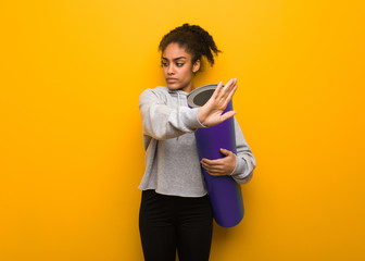 Young fitness black woman putting hand in front. Holding a mat.