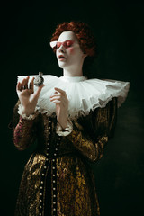 Just a drop. Medieval redhead young woman in golden vintage clothing as a duchess in red sunglasses...
