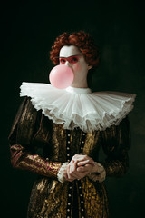 Medieval redhead young woman in golden vintage clothing as a duchess with red sunglasses blowing a...