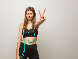Young fitness russian woman showing number two. Holding a jump rope.