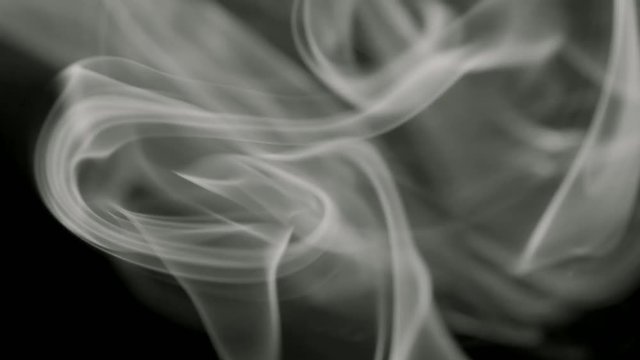 Thin trickle of gray smoke slowly rising graceful twists up on black background. Black and white smoke blowing from bottom to top. Closeup