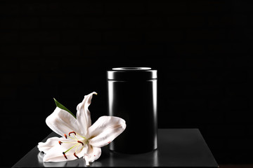 Mortuary urn with lily flower on table against dark background