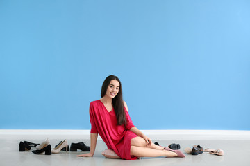 Happy young woman with stylish shoes sitting on floor near color wall