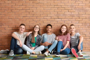 Fotobehang Group of teenagers sitting on floor near brick wall © Pixel-Shot