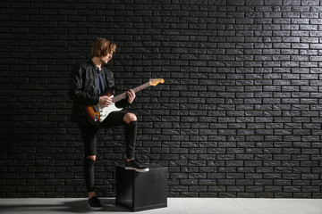 Handsome young man playing guitar against dark brick wall