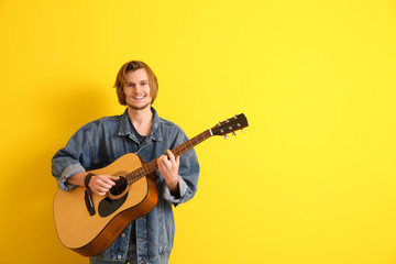 Handsome young man playing guitar on color background