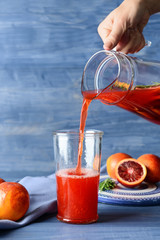 Woman pouring fresh blood orange juice from jug into glass on table