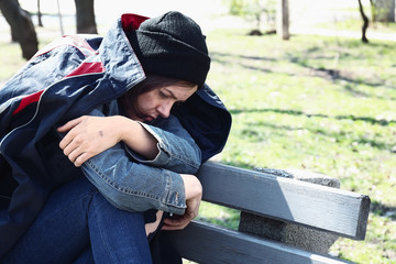 Poor homeless woman sitting on bench outdoors
