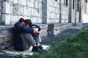 Poor homeless man sitting near wall outdoors