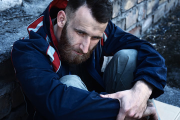 Poor homeless man sitting near wall outdoors