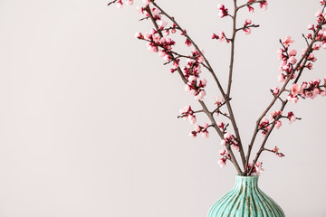 Vase with beautiful blossoming branches on light background